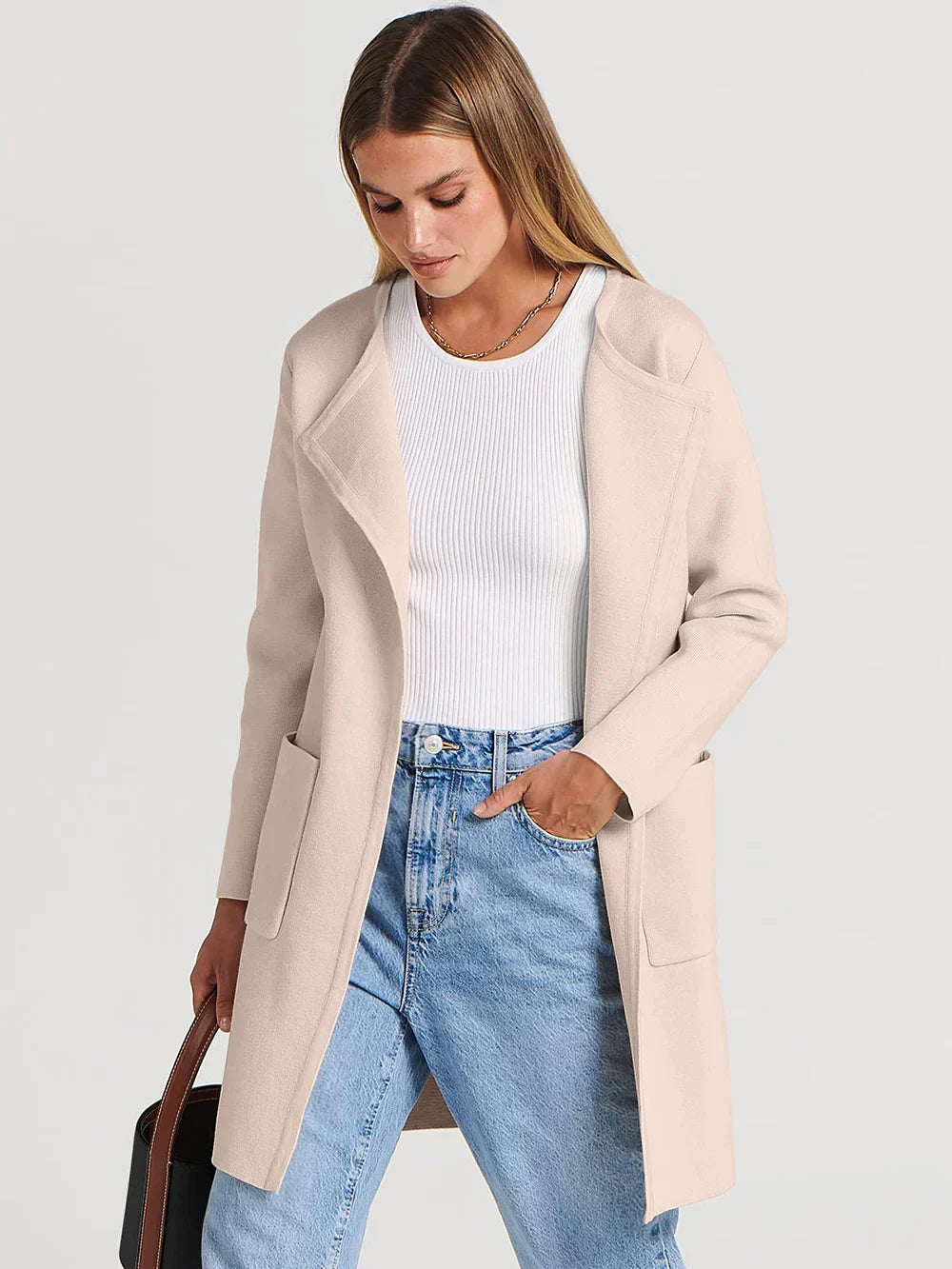 Frau in beigem Mantel, weißem Oberteil und blauer Jeans, modisch, lässig, Herbstmode.