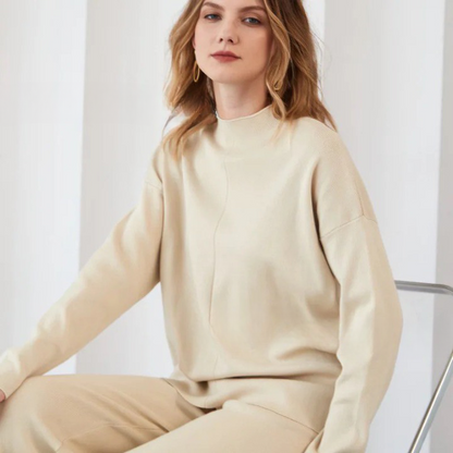 Frau in cremefarbenem Pullover und Hose, sitzt auf Stuhl, minimalistische Mode.