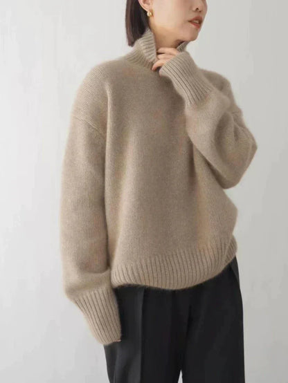 Frau in beigem Strickpullover, Rollkragen, lange Ärmel, schwarze Hose, modisch, elegant.