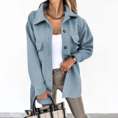 Frau in blauer Wolljacke, weißem Top, beigen Hosen, hält karierte Handtasche.