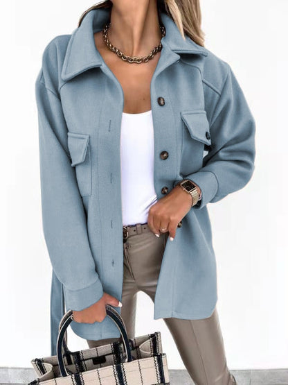 Frau in hellblauer Wolljacke, weiße Bluse, beige Hose, kariertes Handtasche, modisch elegant.