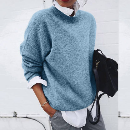 Frau in blauem Strickpullover, weißem Hemd, grauer Hose, hält schwarze Tasche, lässiger Stil.
