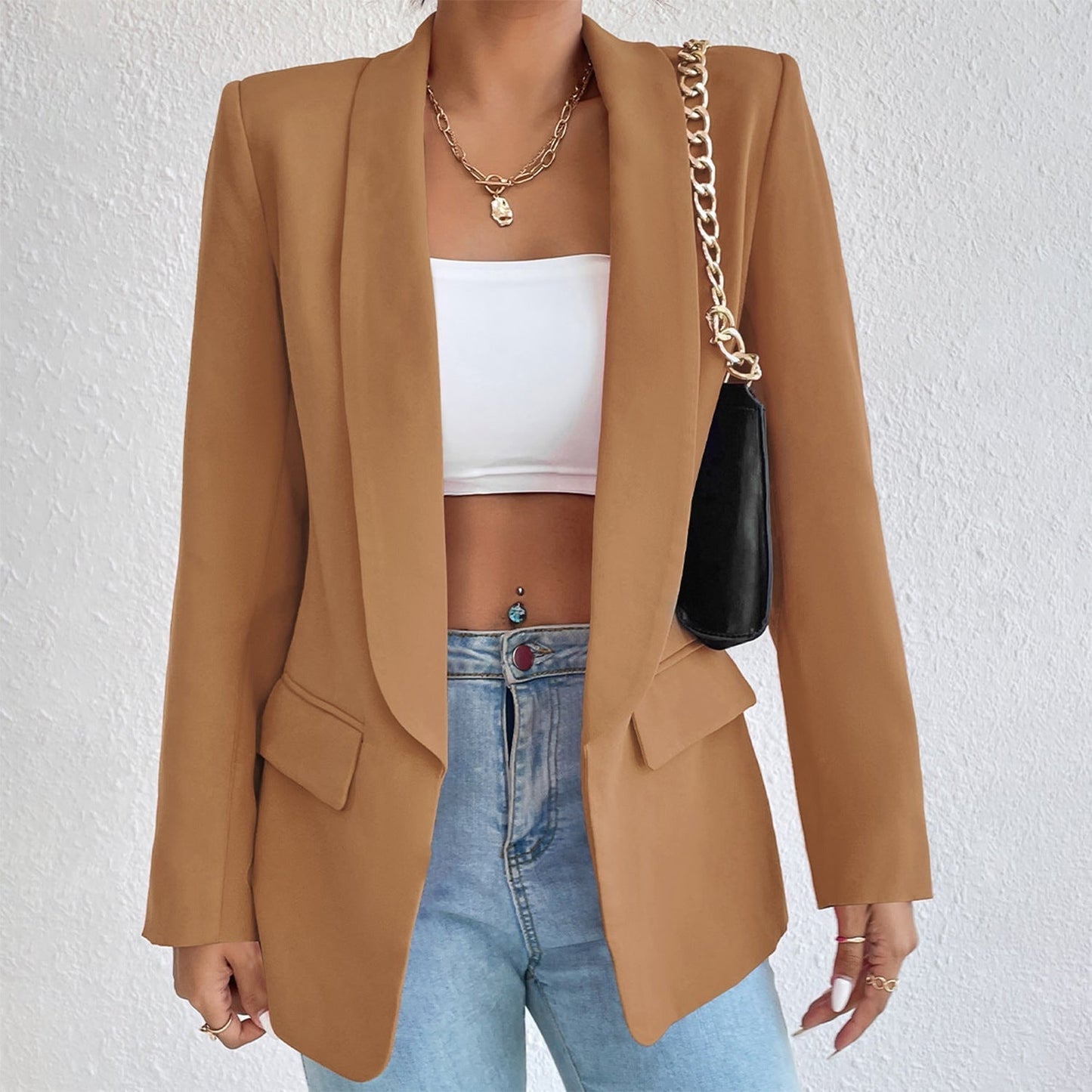 Frau in braunem Blazer, weißem Top, blauer Jeans, schwarze Tasche, goldene Kette.