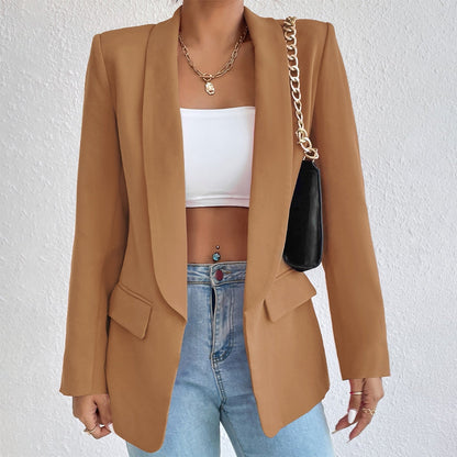 Frau in braunem Blazer, weißem Top, blauer Jeans, schwarze Tasche, goldene Kette.