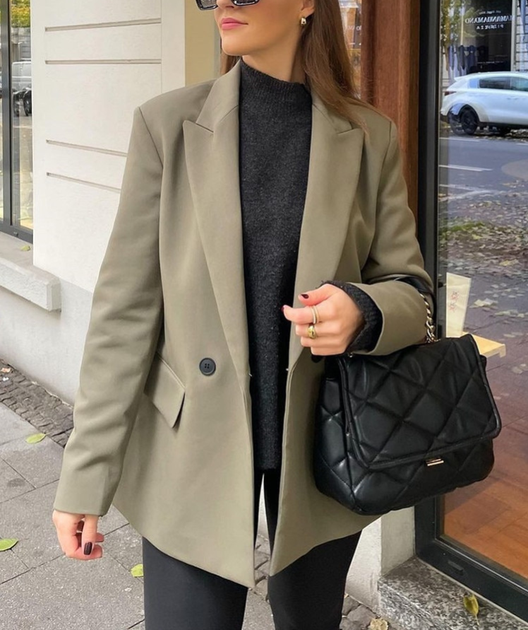 Frau in beigem Blazer mit schwarzer Stepphandtasche auf Straße.