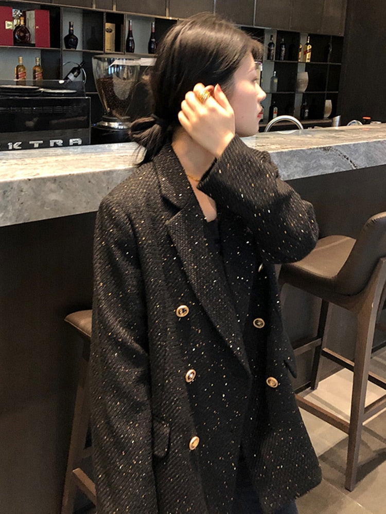 Frau in schwarzem, glitzerndem Blazer mit goldenen Knöpfen in moderner Küche.