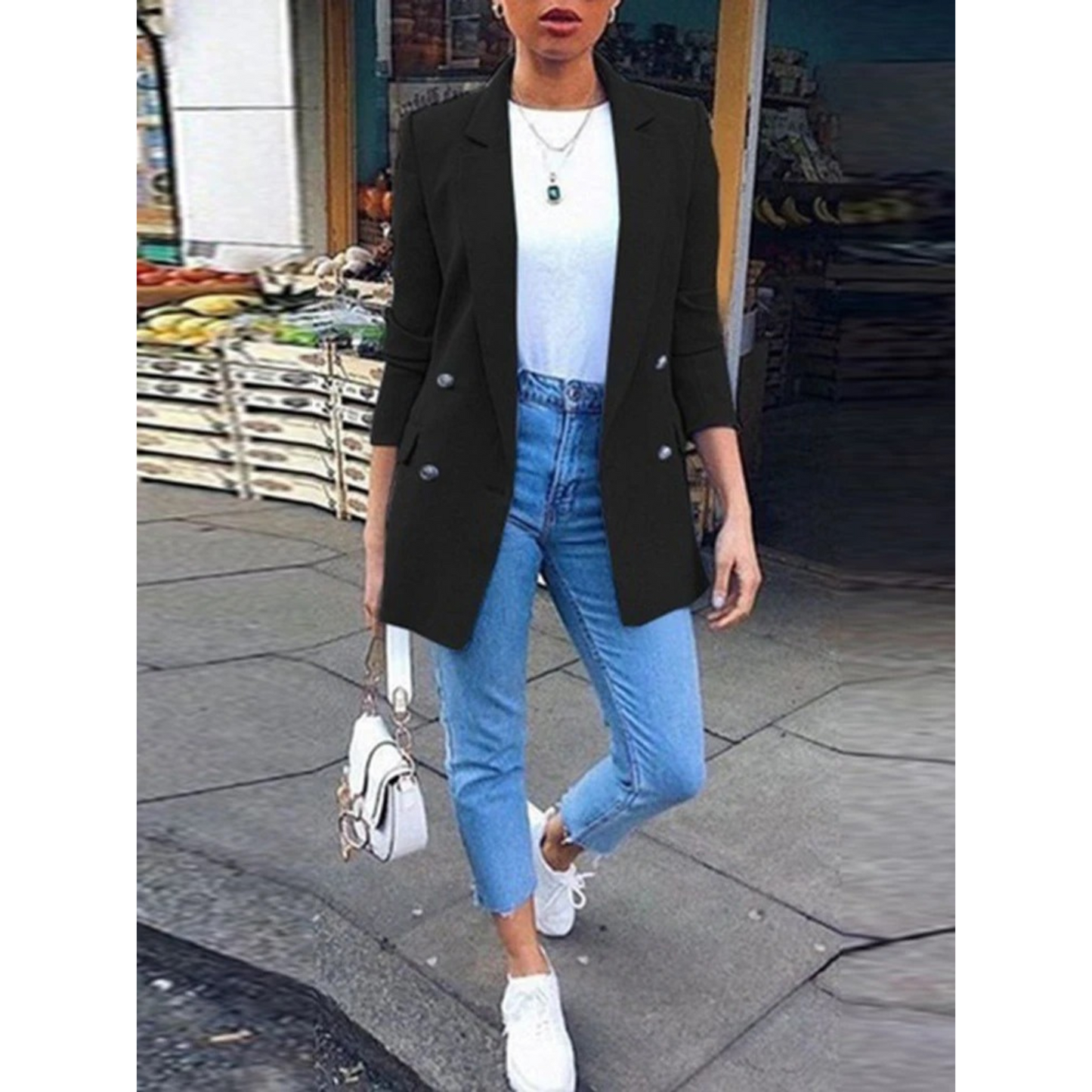Frau in schwarzem Blazer, blauer Jeans und weißen Sneakers auf der Straße.