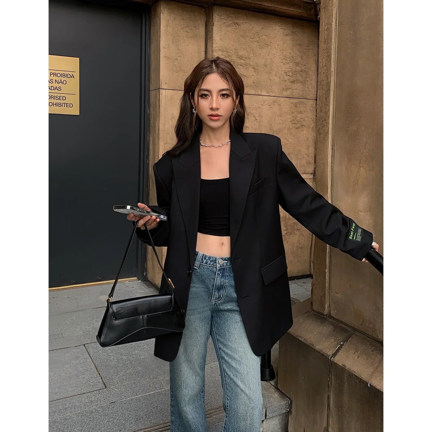 Frau in schwarzem Blazer, Jeans und schwarzem Top, hält schwarze Handtasche, modischer Look.