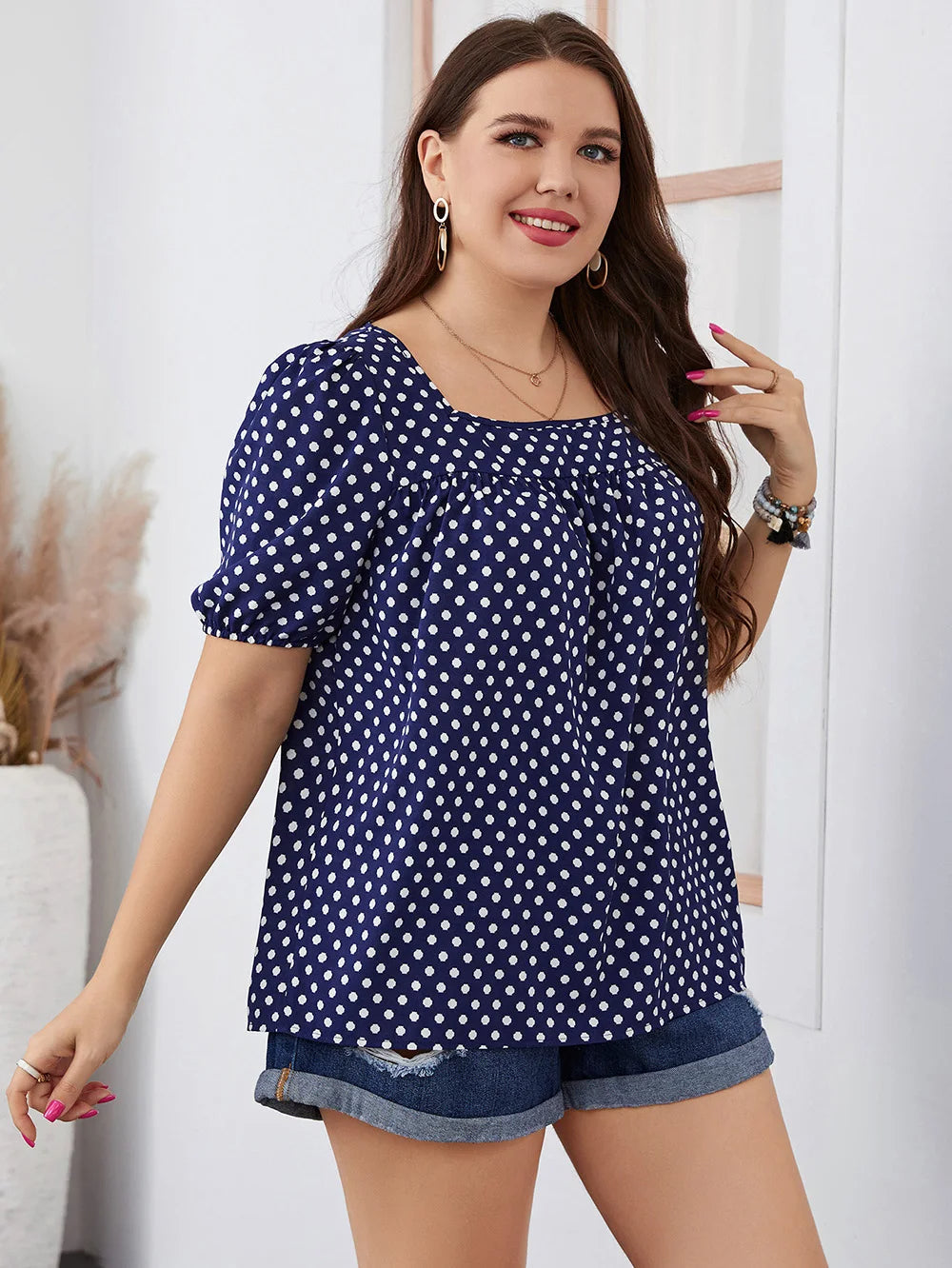 Frau in blauer gepunkteter Bluse und Jeansshorts, lächelnd, modisch, Sommeroutfit.