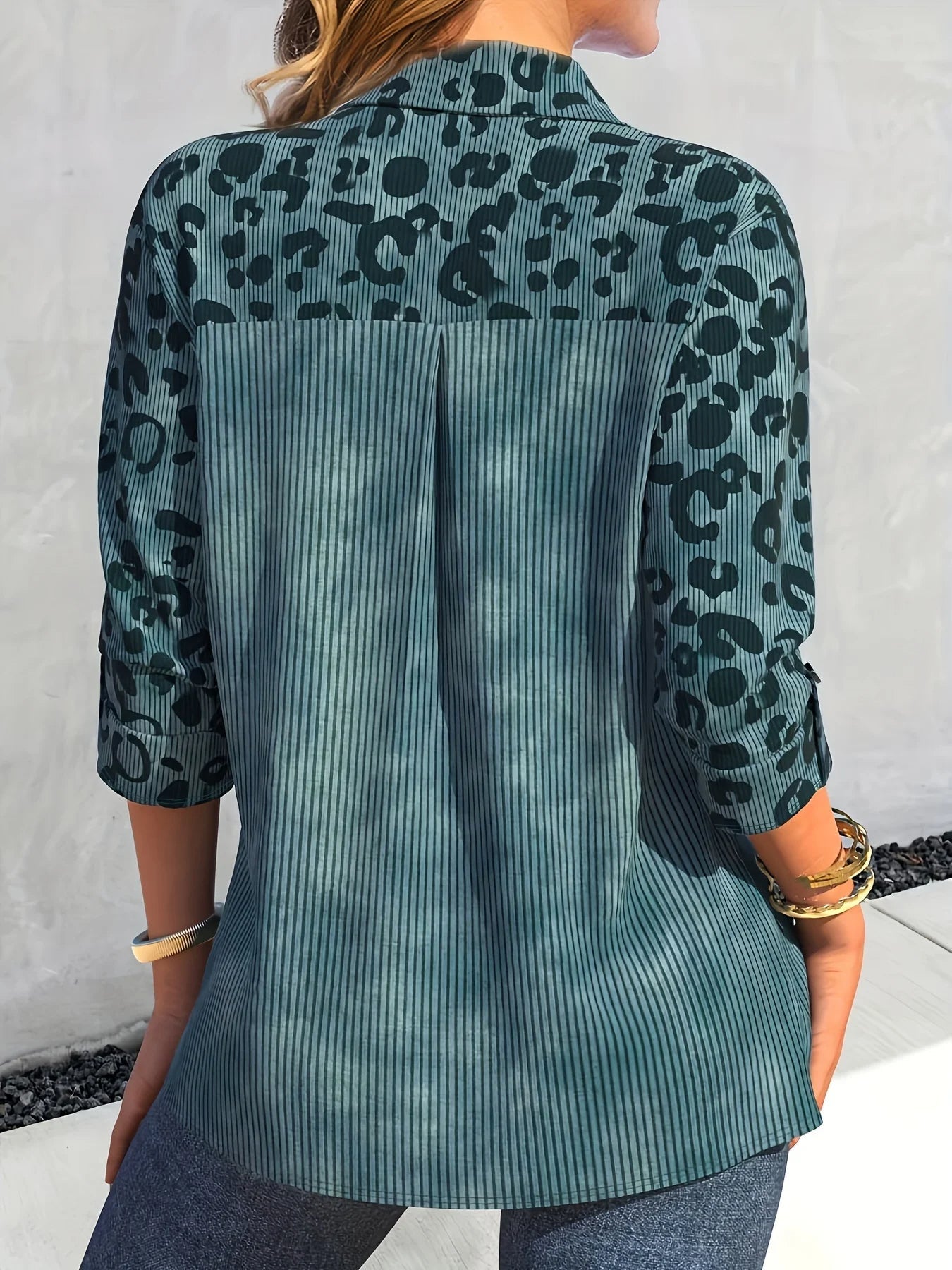 Frau in blau-grünem, gemustertem Hemd mit 3/4-Ärmeln und Jeans von hinten.