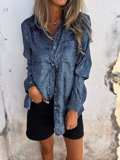Frau in blauer Seidenbluse und schwarzer Shorts vor weißer Wand.