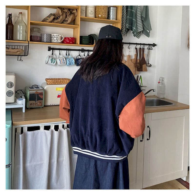 Frau in dunkelblauer Jacke mit braunen Ärmeln in moderner Küche, Rückansicht.