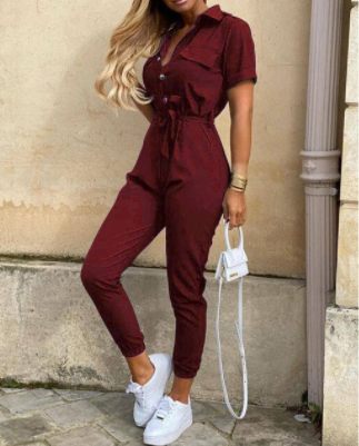 Frau in bordeauxrotem Jumpsuit, weiße Sneaker, kleine weiße Handtasche, modisch, elegant.