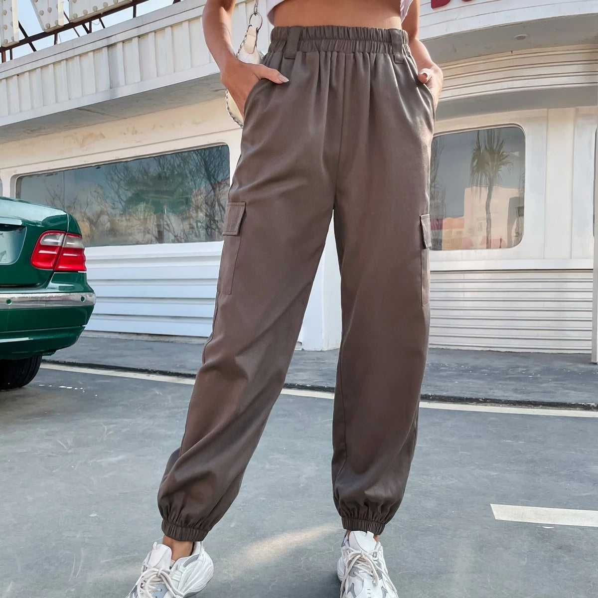 Frau trägt braune, bequeme, hochtaillierte Hose mit Taschen, lässiger Stil, Straße im Hintergrund.