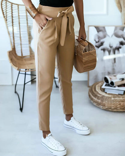 Frau in beigen Paperbag-Hosen, weiße Sneakers, Rattan-Tasche, modisch, lässiger Stil.