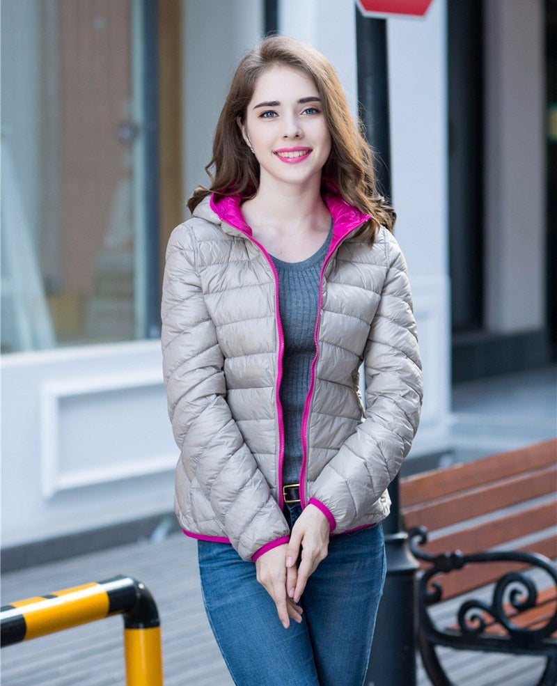 Frau in grauer Daunenjacke mit pinkem Futter, lächelnd, draußen, modisch, Herbstkleidung.