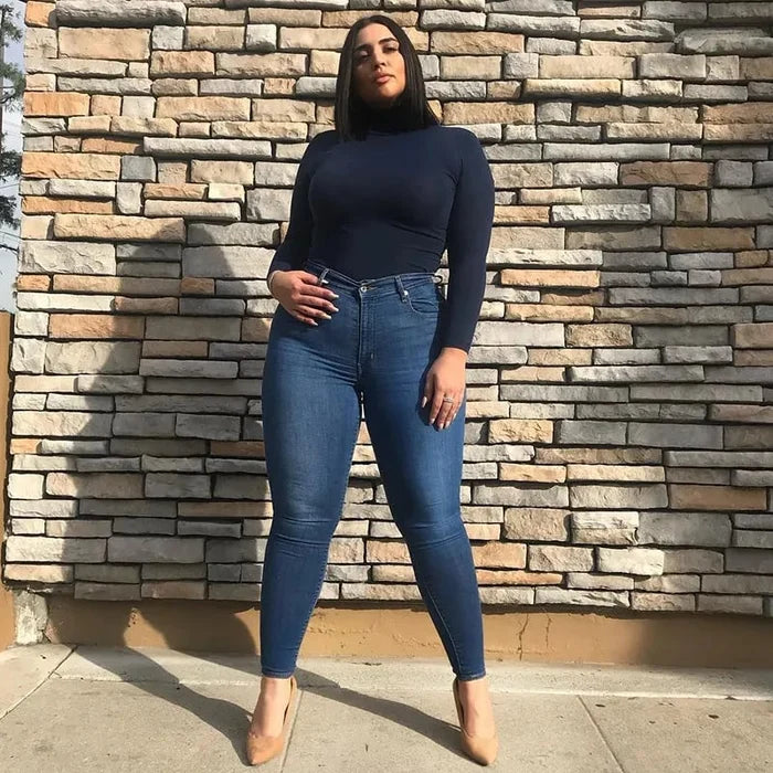 Frau in dunkelblauem Rollkragenpullover und blauen Jeans vor Ziegelwand, Mode, Streetstyle.