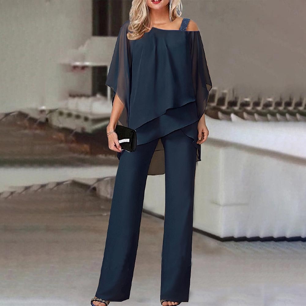 Frau in eleganter, dunkelblauer Chiffon-Hose und Bluse, Abendmode, schulterfrei, mit Clutch.