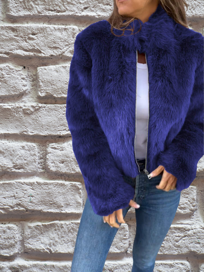 Frau in blauer Kunstpelzjacke vor Ziegelwand, modisch, warm, Winterbekleidung.