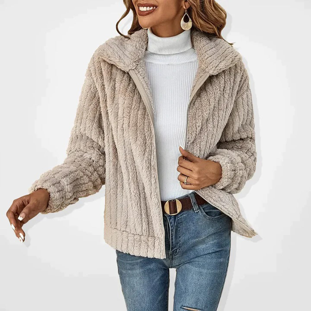 Frau in beiger Kunstpelzjacke, weißem Rollkragenpullover und blauer Jeans, lächelnd.