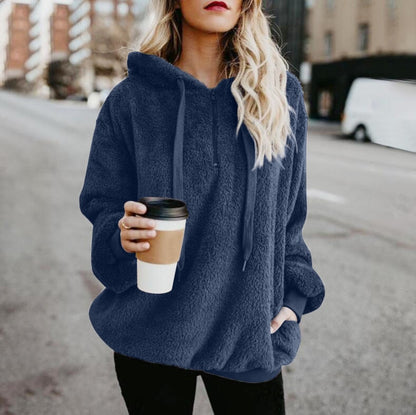 Frau in blauem Fleece-Hoodie hält Kaffeebecher, Straßenhintergrund, lässige Wintermode.