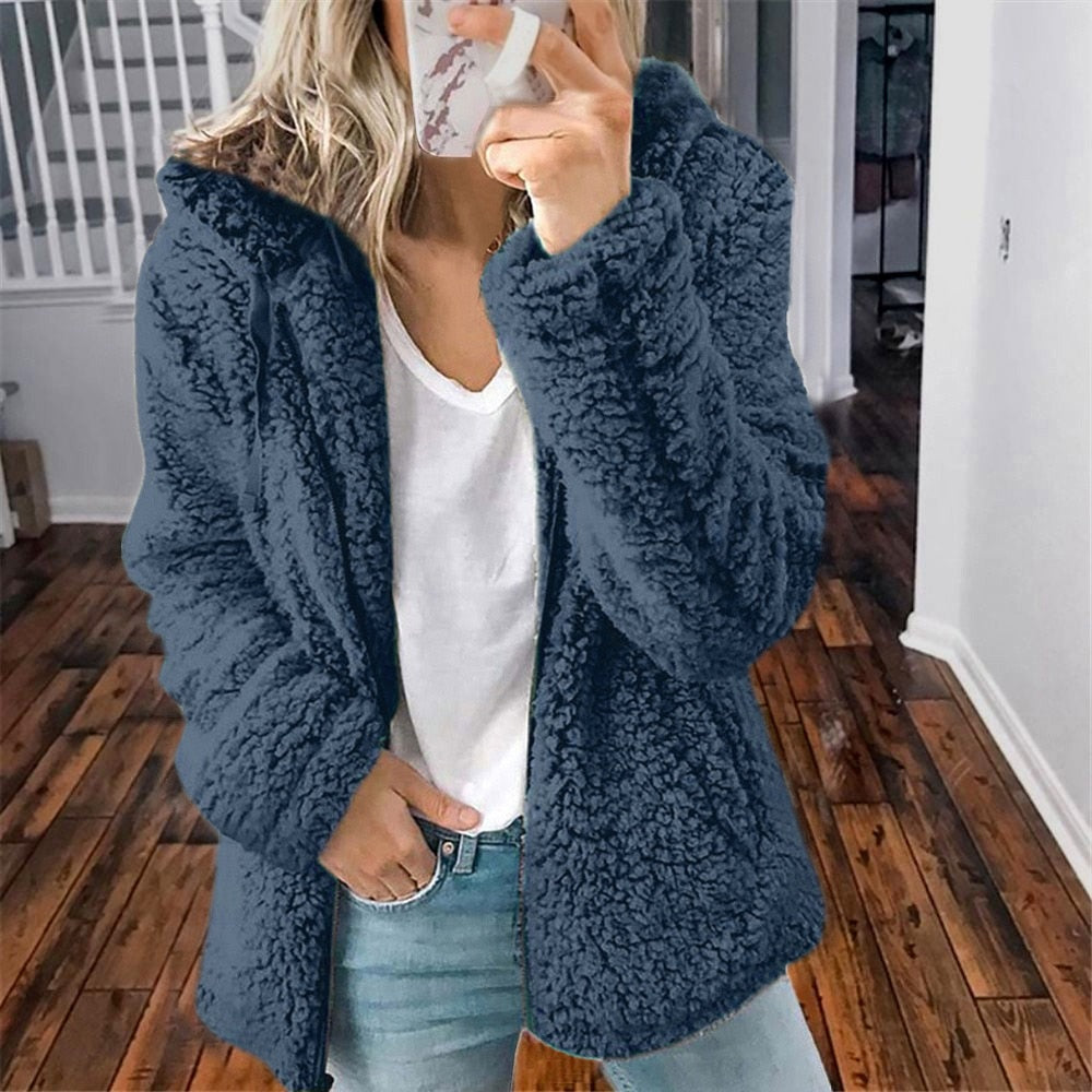 Frau in blauer Teddyjacke, weißem T-Shirt und Jeans, gemütlicher Winterlook, Holzboden.