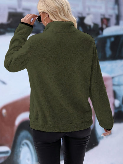 Frau in olivgrüner Fleecejacke, schwarze Lederhose, Sonnenbrille, Stadt im Hintergrund.
