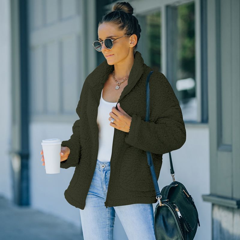 Frau in schwarzer Teddyjacke, Sonnenbrille, Jeans, hält Kaffeebecher, modisch, urban.