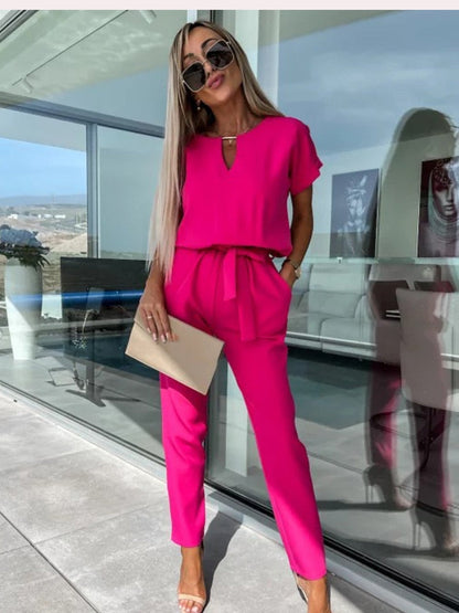Frau in pinkem Jumpsuit mit Sonnenbrille und Clutch auf Terrasse, modisch, elegant, Sommeroutfit.