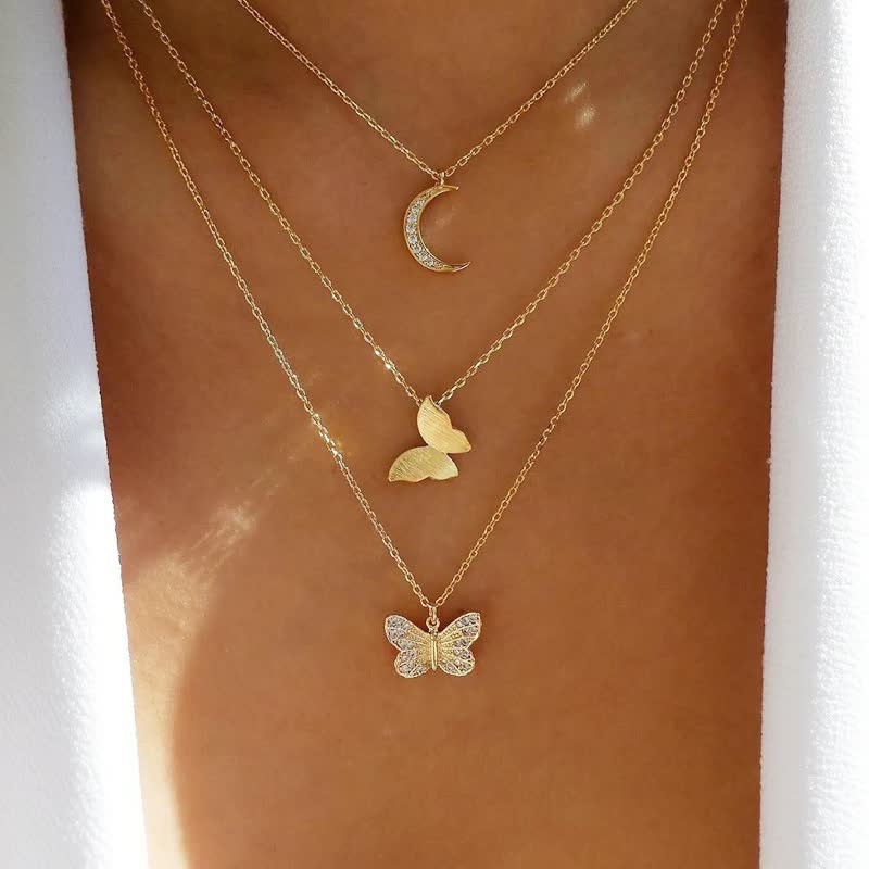 Dreifache goldene Halskette mit Mond- und Schmetterlingsanhängern auf Haut.
