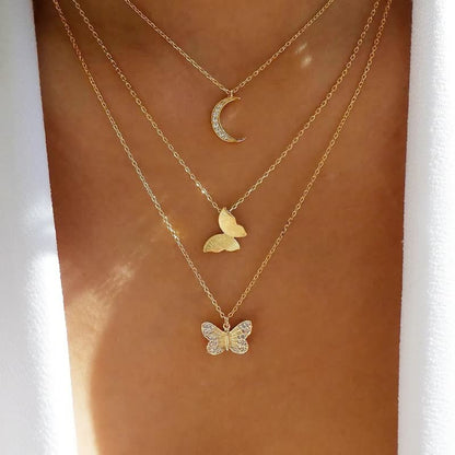 Dreifache goldene Halskette mit Mond- und Schmetterlingsanhängern auf Haut.
