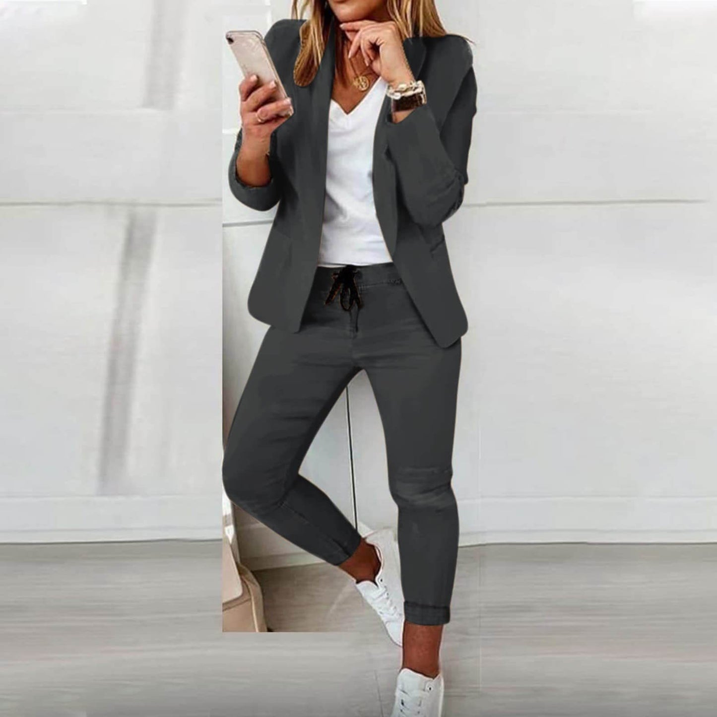 Frau im grauen Anzug mit Smartphone, weißem T-Shirt und Sneakers, Business-Casual-Look.