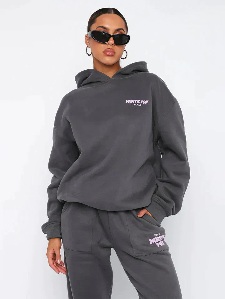 Frau in grauem Hoodie und Jogginghose, Sonnenbrille, lässige Mode, Streetwear-Look.