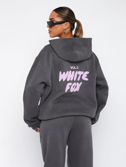 Frau in grauem Hoodie mit "White Fox" Aufdruck, Sonnenbrille, lässiger Stil, Streetwear-Mode.