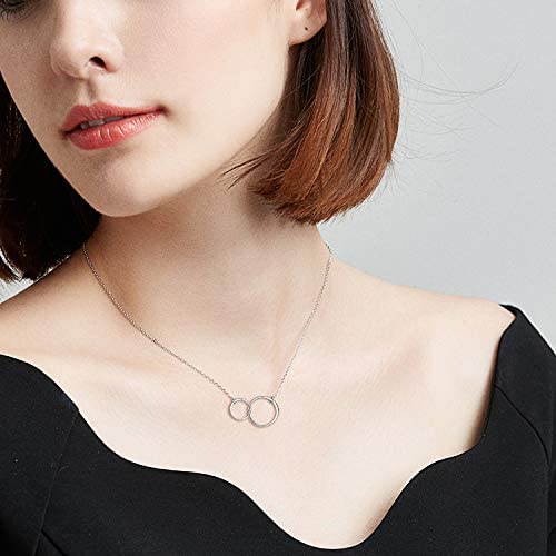Frau mit silberner Halskette, zwei verbundene Ringe, elegantes Schmuckdesign, Nahaufnahme.