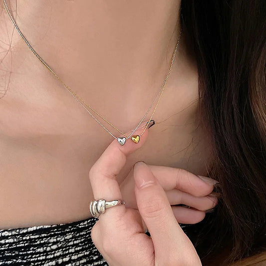 Frau trägt zweifarbige Herz-Halskette, Silber und Gold, modisches Schmuckdesign.