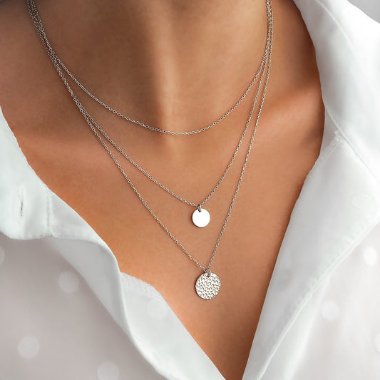 Dreifache Silberhalskette mit runden Anhängern auf weißer Bluse, eleganter Schmuck.