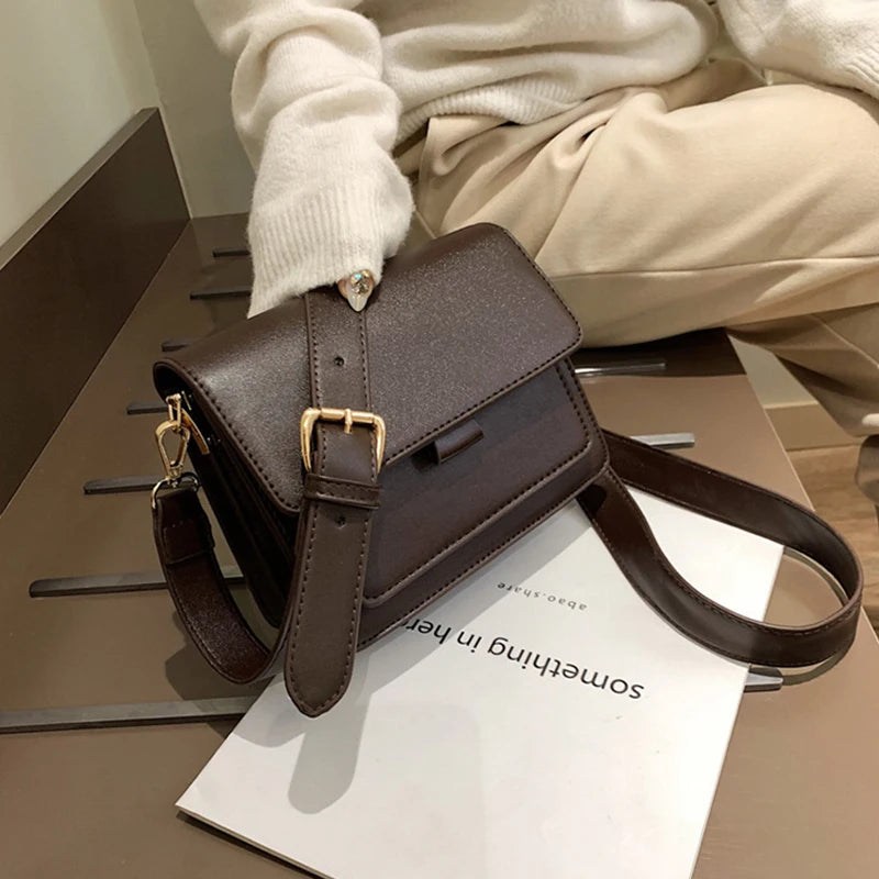 Dunkelbraune Lederhandtasche mit goldener Schnalle auf Tisch, modisch, elegant, Damenaccessoire.