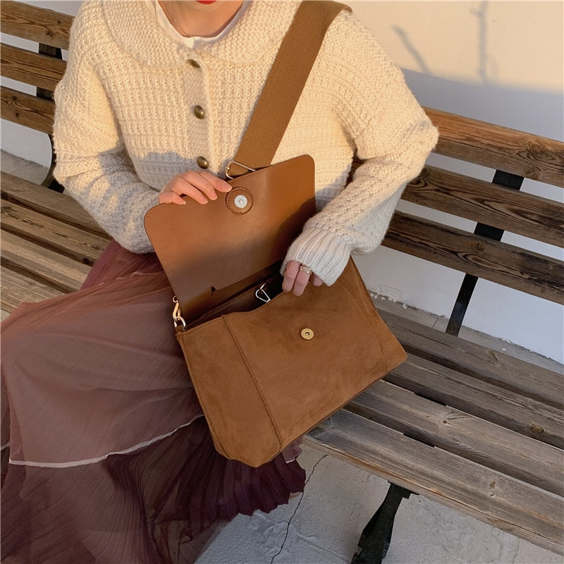 Frau mit brauner Umhängetasche aus Leder auf Holzbank, Herbstmode, Strickjacke, Plisseerock.