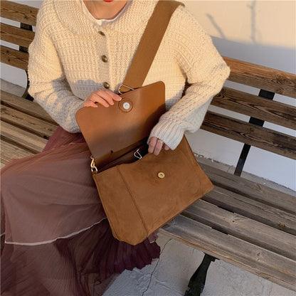 Frau mit brauner Umhängetasche aus Leder auf Holzbank, Herbstmode, Strickjacke, Plisseerock.