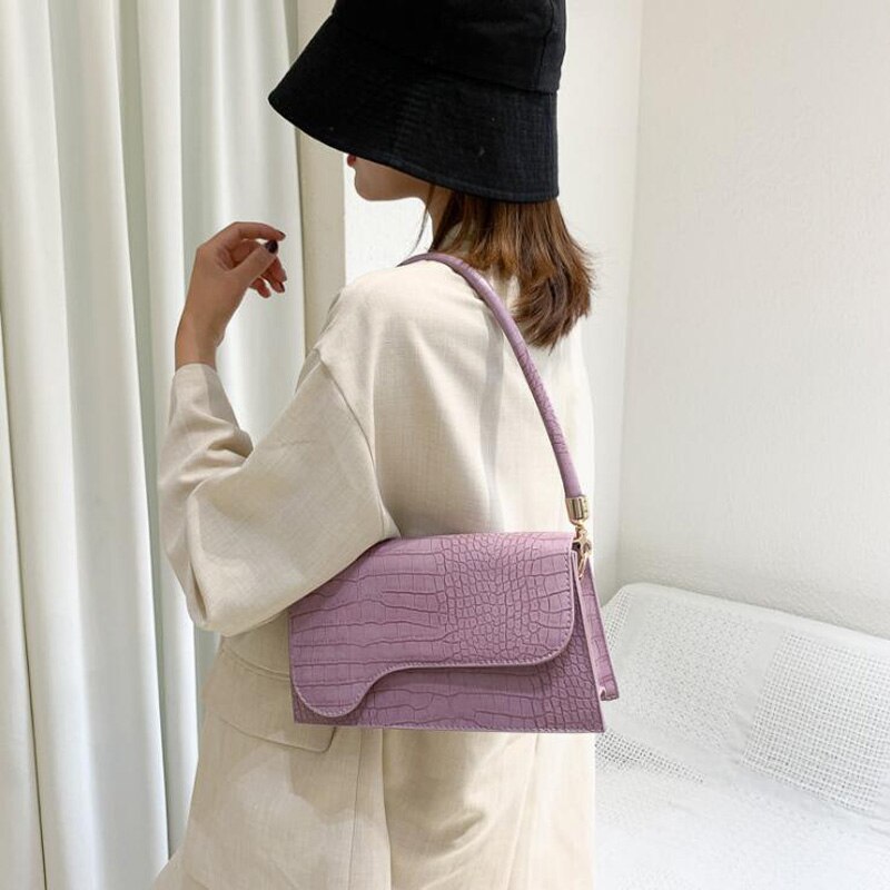 Frau mit lila Krokodilleder-Handtasche, schwarzem Hut, beiger Jacke, modisch, elegant.