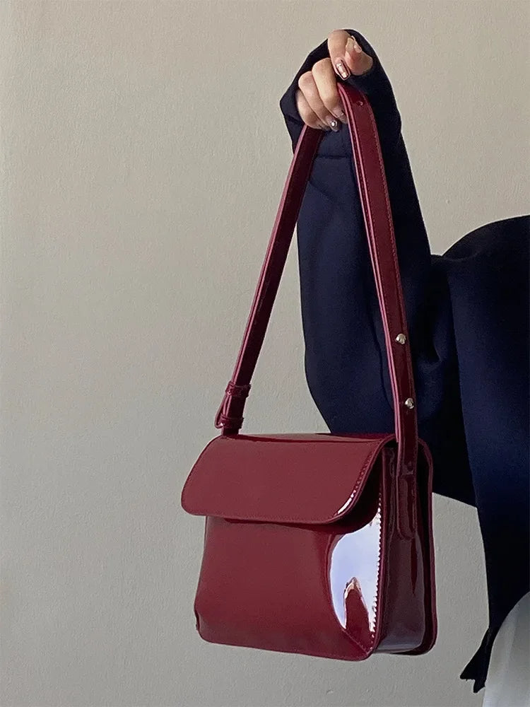 Dunkelrote, glänzende Handtasche aus Leder, rechteckig, mit verstellbarem Riemen, elegant.