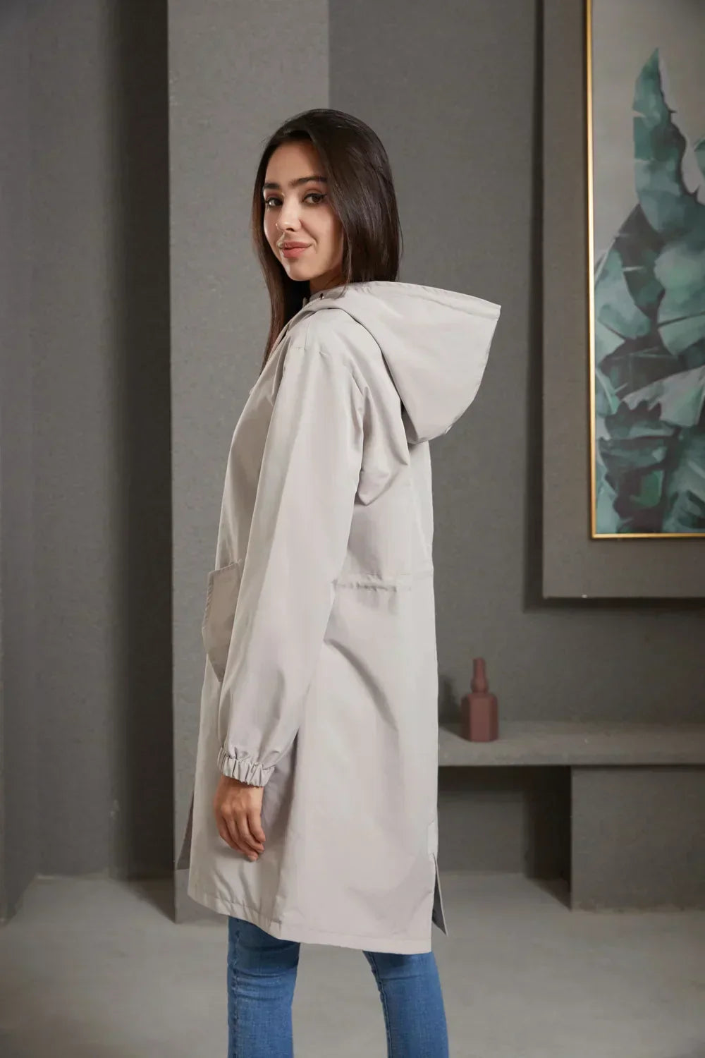 Frau in grauem Kapuzenmantel, lässig, modern, Herbstmode, Damenbekleidung, seitlich stehend.