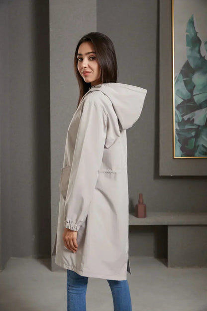 Frau in grauem Kapuzenmantel, lässig, modern, Herbstmode, Damenbekleidung, seitlich stehend.