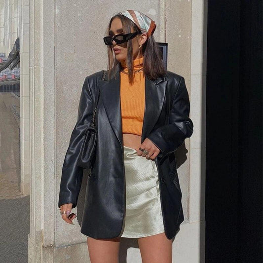 Frau in schwarzem Lederblazer, orangefarbenem Oberteil, weißem Rock, Sonnenbrille, Herbstmode.