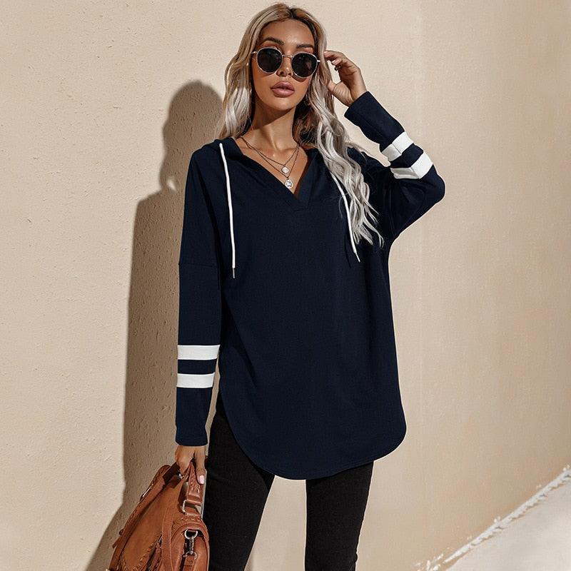 Frau in dunkelblauem Hoodie mit Streifen, Sonnenbrille, braune Tasche, lässige Mode.