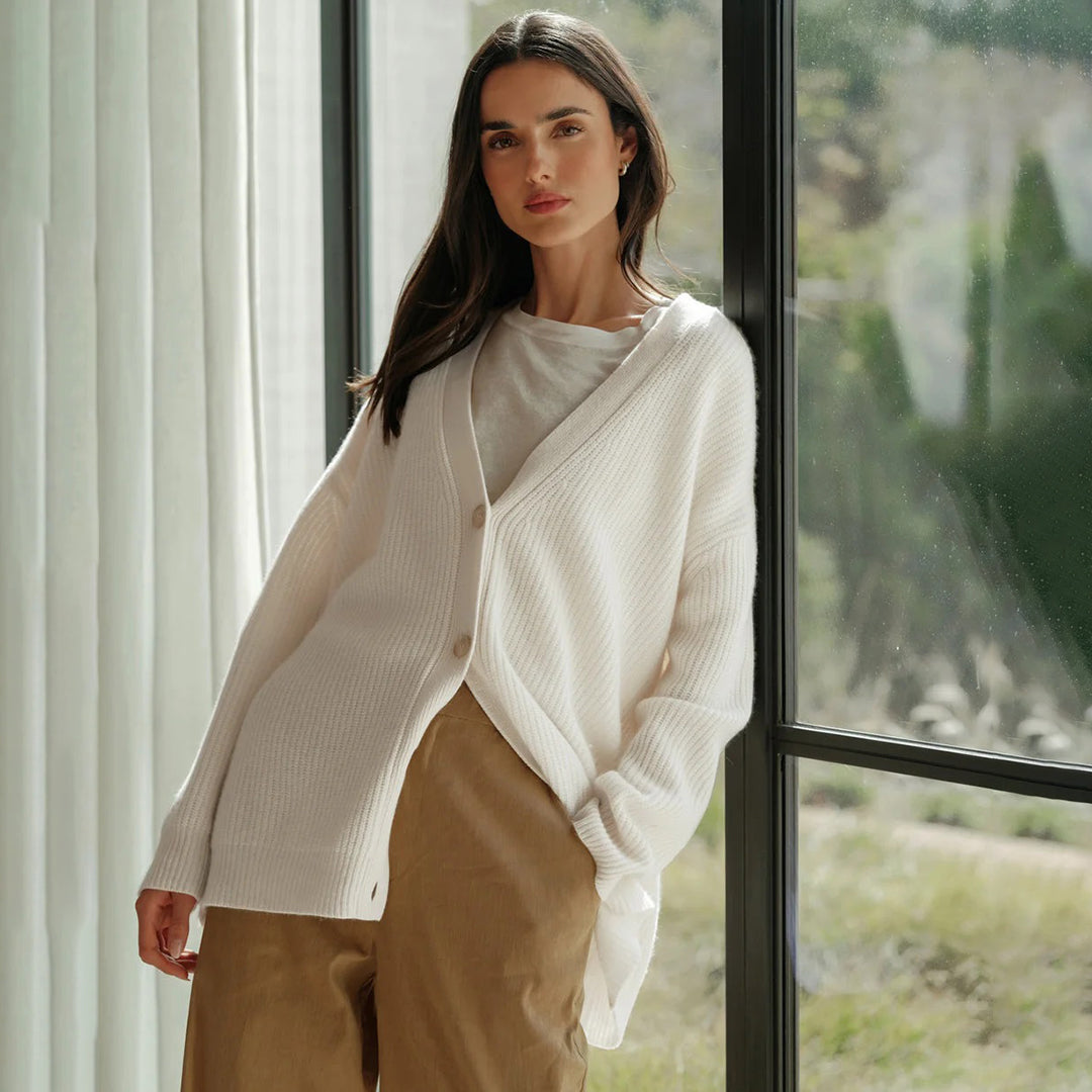 Frau trägt weißen Strick-Cardigan, lässig, elegant, vor Fenster stehend, Herbstmode.