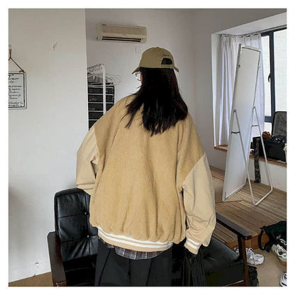 Person in beiger Oversize-Jacke und Cap in modernem Wohnzimmer mit Spiegel und Ledersessel.