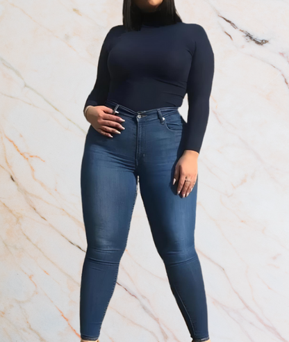 Frau in dunkelblauem Rollkragenpullover und Jeans vor Marmorhintergrund.