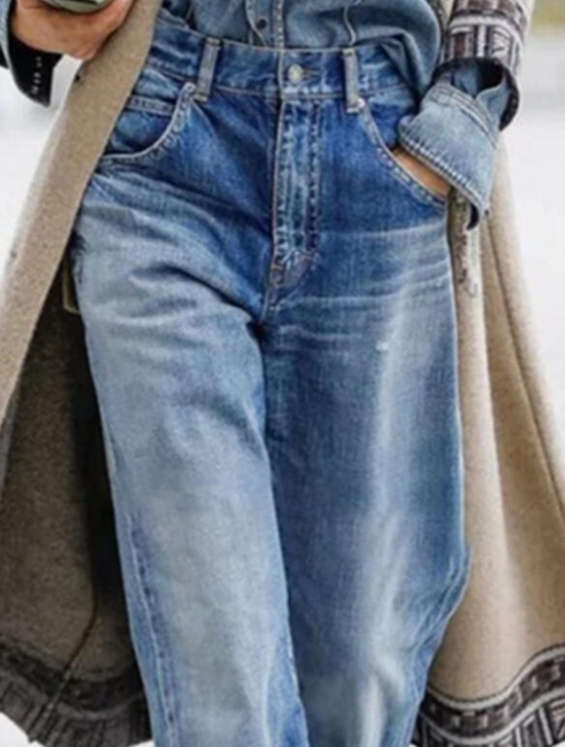 Person in blauer Jeans und Jeanshemd, beige Mantel, lässiger Streetstyle-Look.